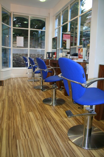 Blue salon chairs lined up along the bay window mirrors